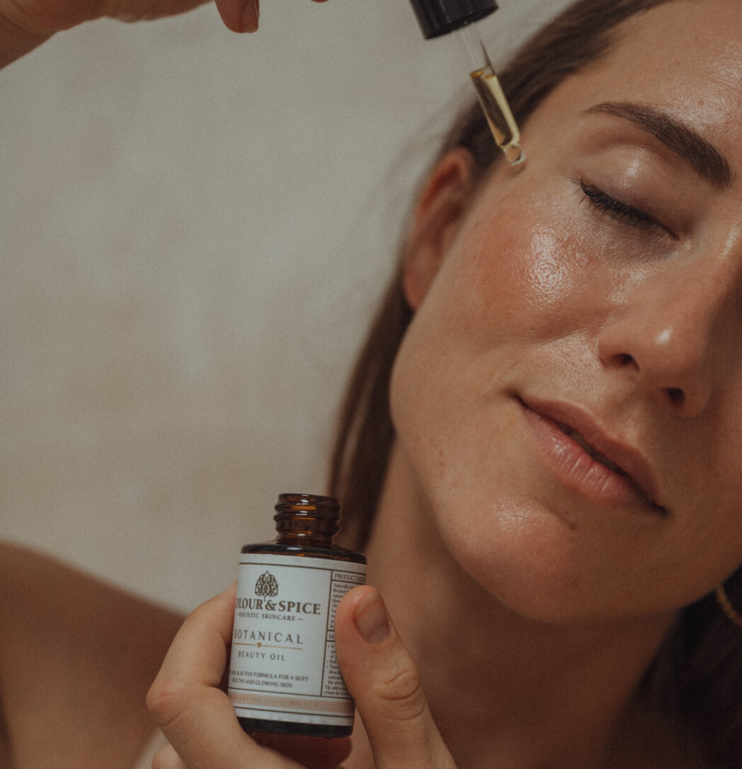 Vrouw die met pipet skincare aanbrengt op haar gezicht van beauty brand Colour&Spice. Ze draagt in haar andere hand een flesje Botanical beauty oil