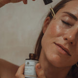 Vrouw die een flesje Colour and Spice Botanical Beauty oil vasthoudt en gezichtsolie met een pipet aanbrengt op haar gezicht.