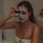 Vrouw die Colour and Spice gezichtsmasker heeft aangebracht en het potje voor haar oog houdt, in een wellness setting.
